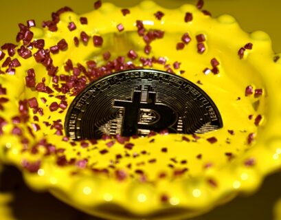 Eine Bitcoin-Münze liegt in einer gelben Schale, umgeben von rosa Zuckerkristallen.