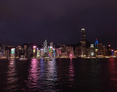Blick auf die beleuchtete Skyline von Hongkong mit Wolkenkratzern und Wasserreflexionen.