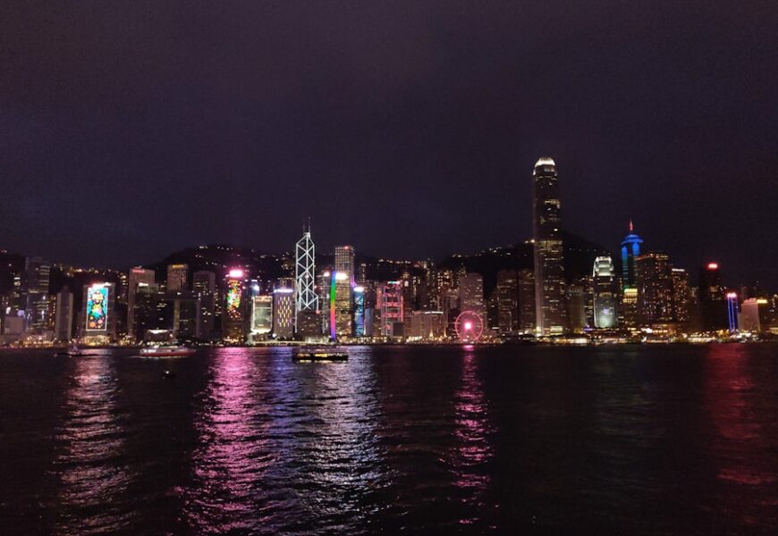 Blick auf die beleuchtete Skyline von Hongkong mit Wolkenkratzern und Wasserreflexionen.