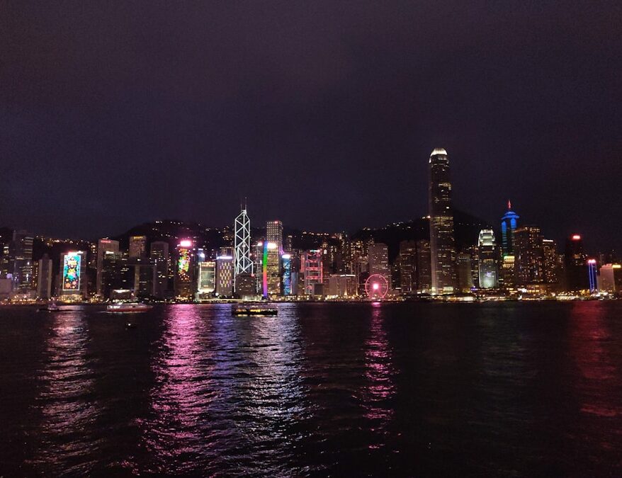 Blick auf die beleuchtete Skyline von Hongkong mit Wolkenkratzern und Wasserreflexionen.