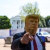 Person trägt eine Donald Trump Maske und zeigt mit dem Finger auf die Kamera vor dem Weißen Haus.