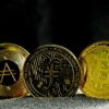 Drei goldene Kryptowährungs-Münzen mit Symbolen für verschiedene digitale Währungen.