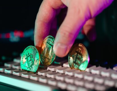 Eine Hand platziert drei Kryptowährungs-Münzen auf einer Computer-Tastatur.