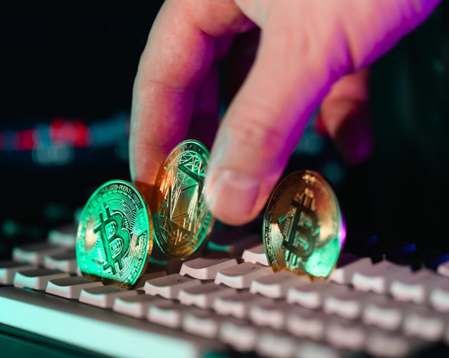 Eine Hand platziert drei Kryptowährungs-Münzen auf einer Computer-Tastatur.